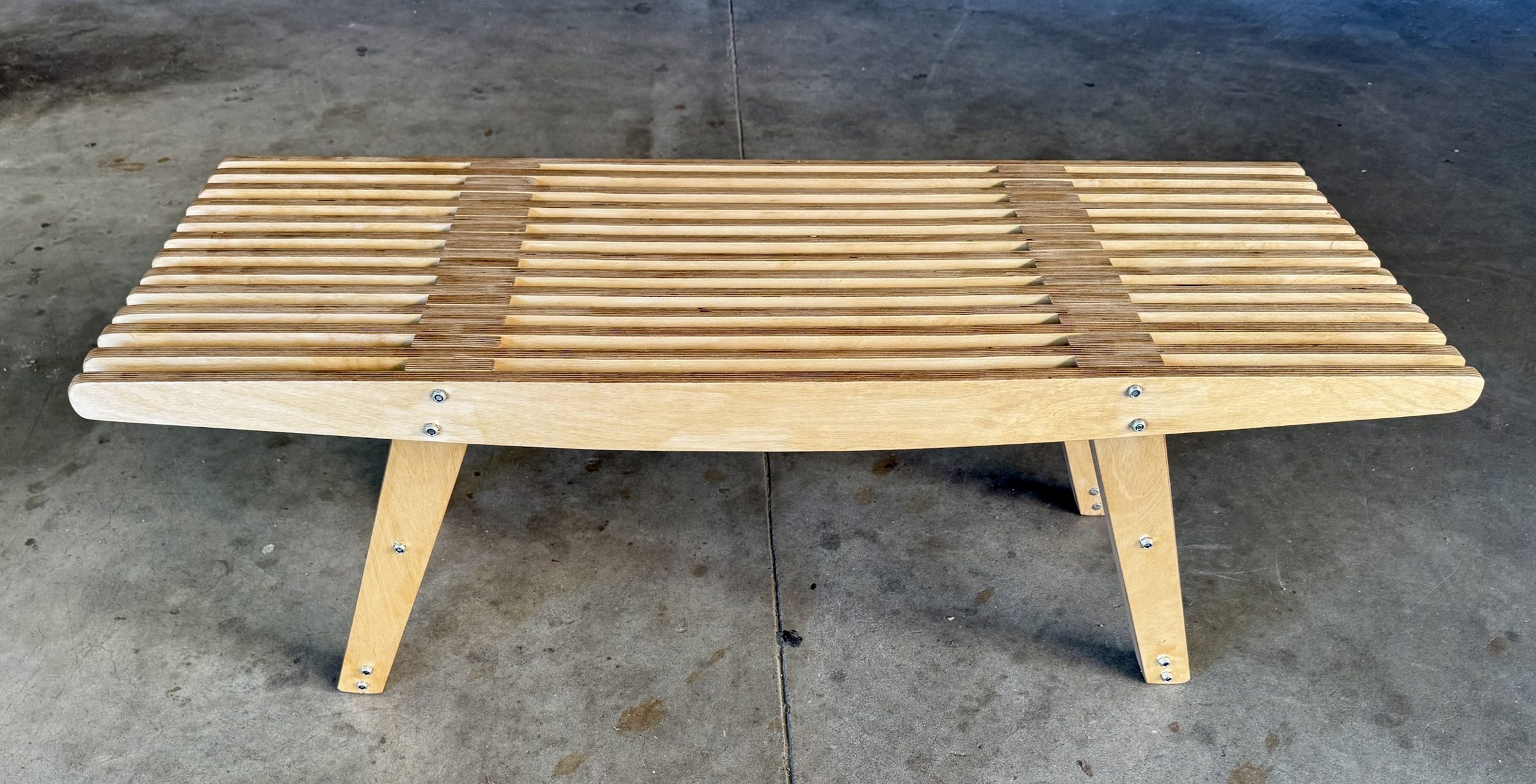 Plywood slat bench seen from the front: curved side rails, splayed legs, bolted joints